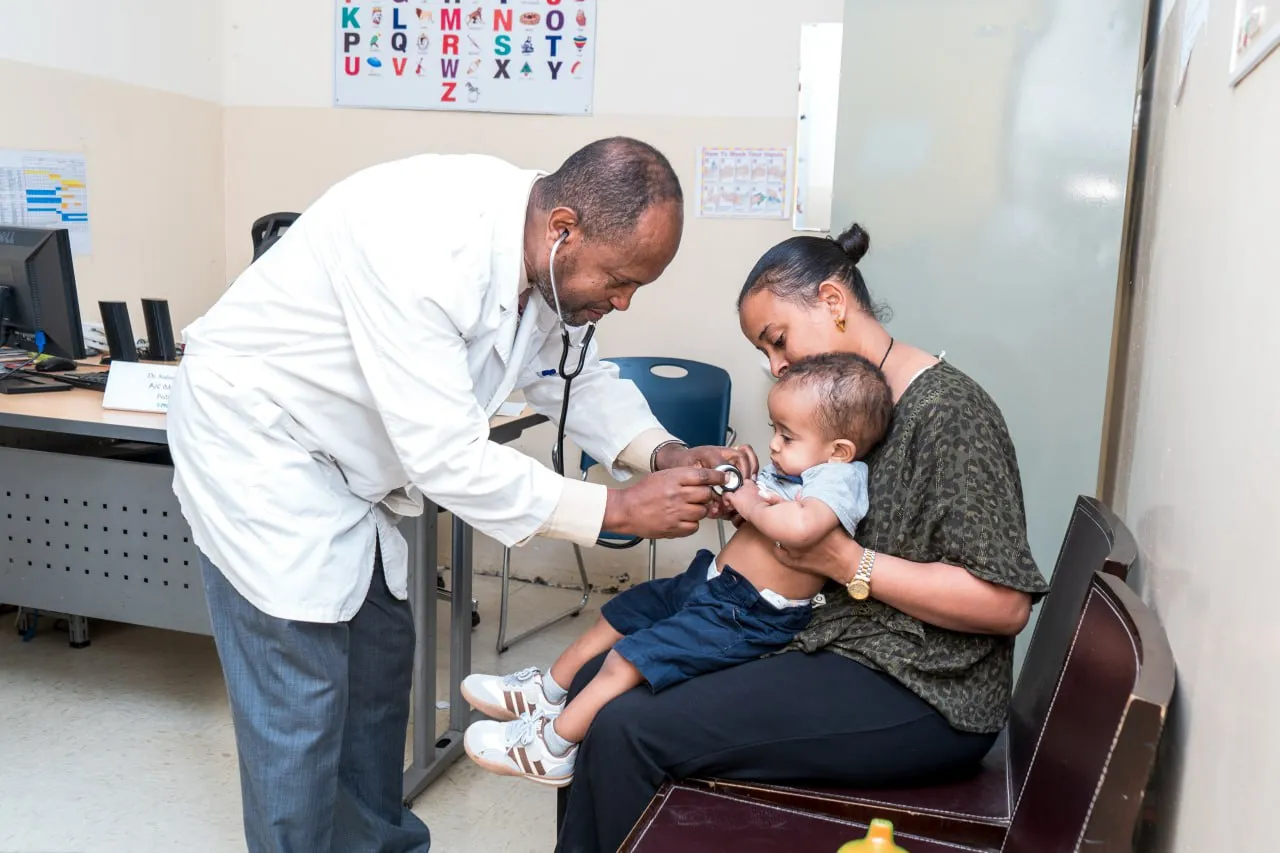 A doctor examines a young child held by their mother